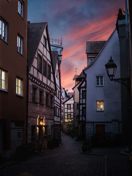 Enge Gasse mit Fachwerkhäusern und bunter Abenddämmerung im Hintergrund.